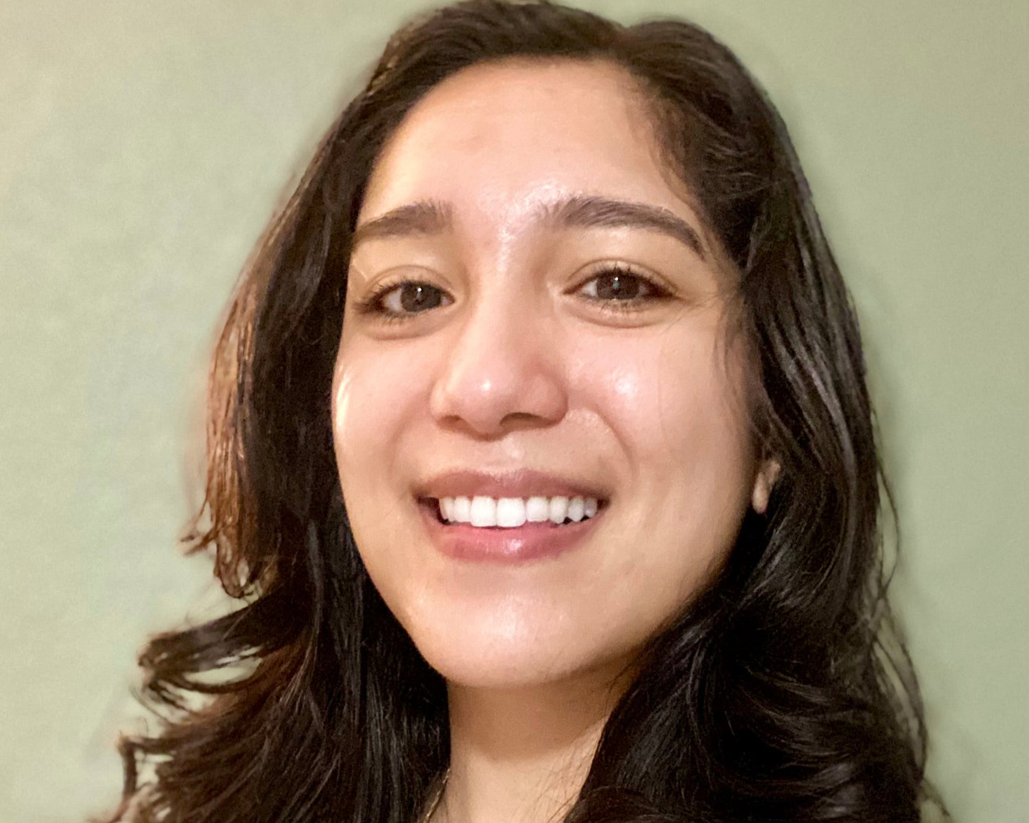 Woman with long dark hair smiling against a plain background